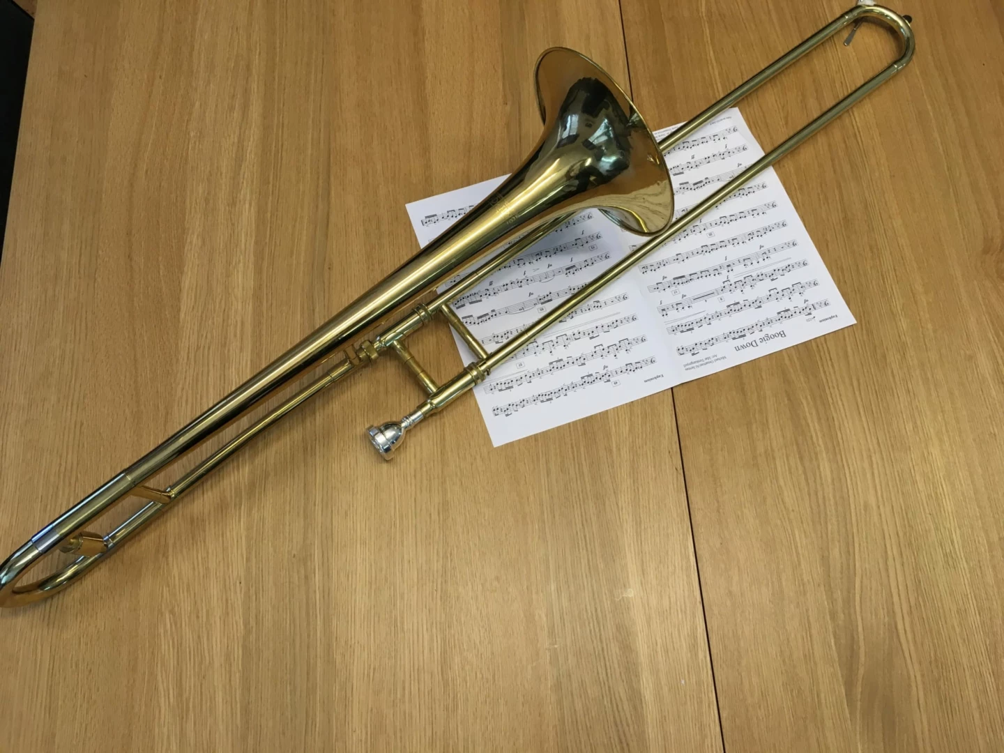Bilden förställer en Trombon som ligger ovanpå ett uppslag notblad på ett träbord.