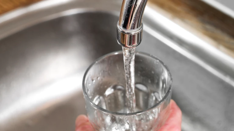 En hand som håller i ett glas och fyller det med vatten från kranen